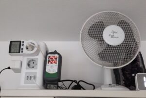 Tischventilator im Regal, links Mehrfachsteckdose mit Temperatur-Regelung